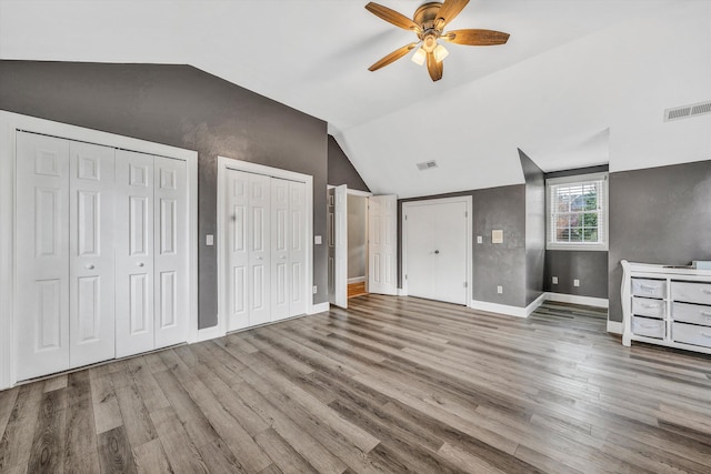 unfurnished bedroom with two closets, visible vents, wood finished floors, and vaulted ceiling