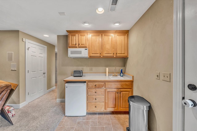 kitchen featuring light countertops, a sink, white microwave, and baseboards