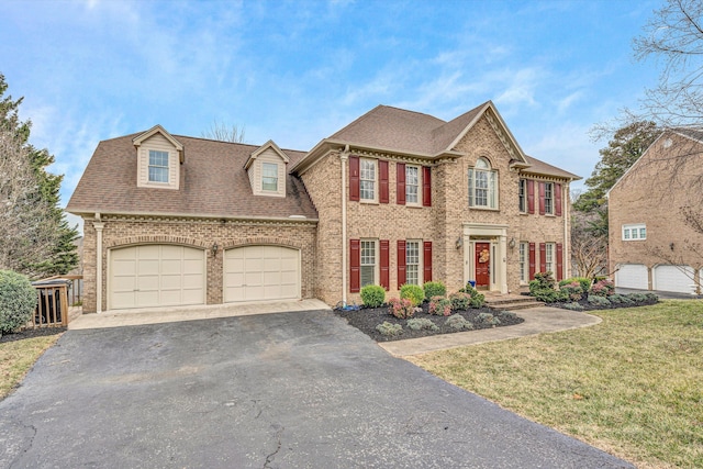 view of front facade featuring an attached garage, brick siding, a front lawn, driveway, and a shingled roof