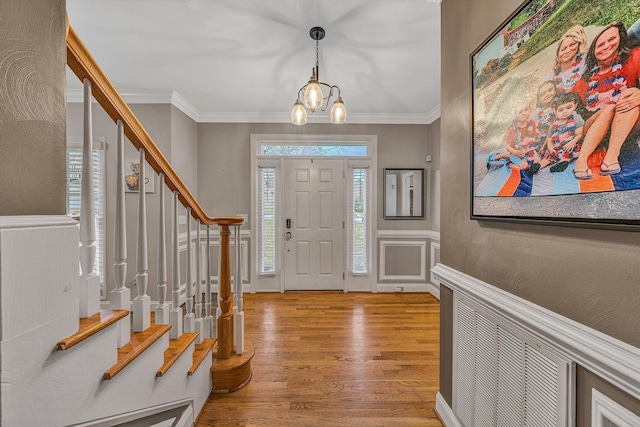 foyer entrance with ornamental molding, stairway, a chandelier, and wood finished floors