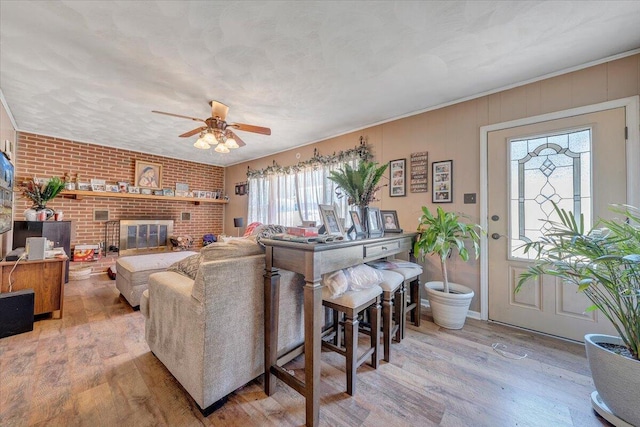 living room featuring brick wall, a fireplace, ornamental molding, ceiling fan, and light hardwood / wood-style flooring