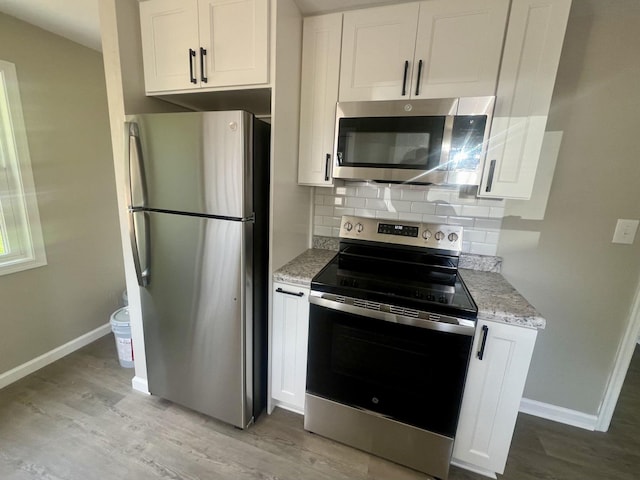 kitchen featuring appliances with stainless steel finishes, white cabinetry, backsplash, light stone countertops, and light hardwood / wood-style floors