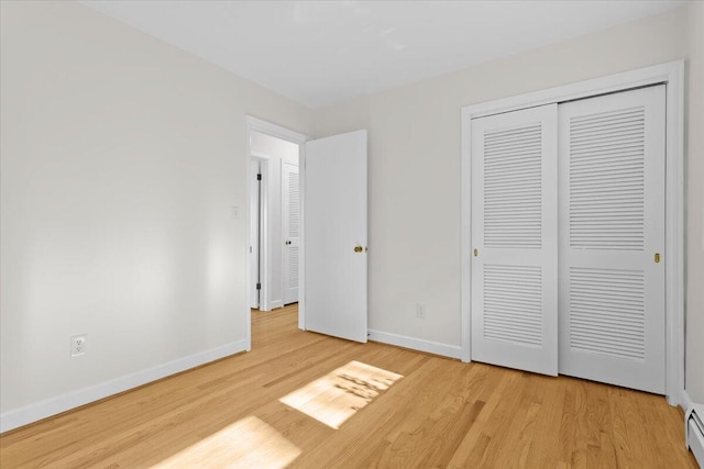 unfurnished bedroom featuring light wood-type flooring, a baseboard radiator, baseboards, and a closet