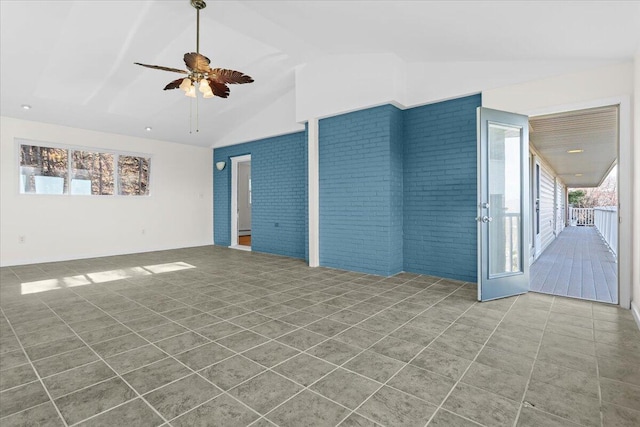 tiled empty room featuring vaulted ceiling, brick wall, and a healthy amount of sunlight