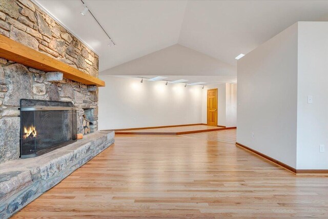 3615 Dogwood Ln SW, Roanoke, VA 24015 - unfurnished living room featuring track lighting, wood finished floors, a stone fireplace, lofted ceiling, and baseboards
