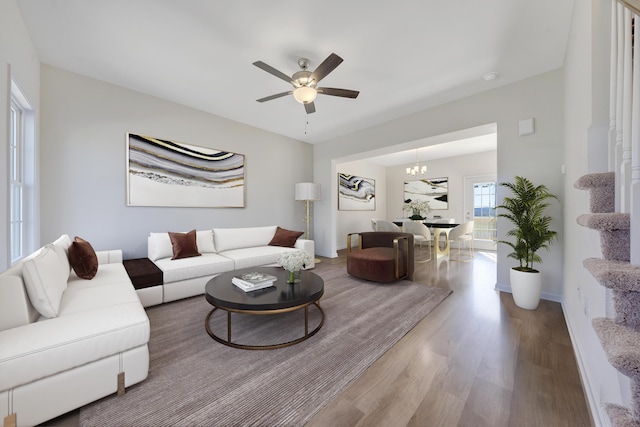 living area featuring ceiling fan with notable chandelier, baseboards, and wood finished floors