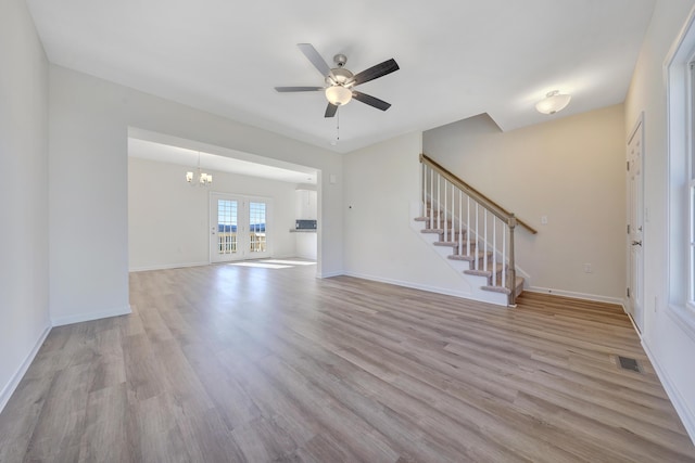 unfurnished living room with baseboards, visible vents, stairs, light wood-style floors, and ceiling fan with notable chandelier