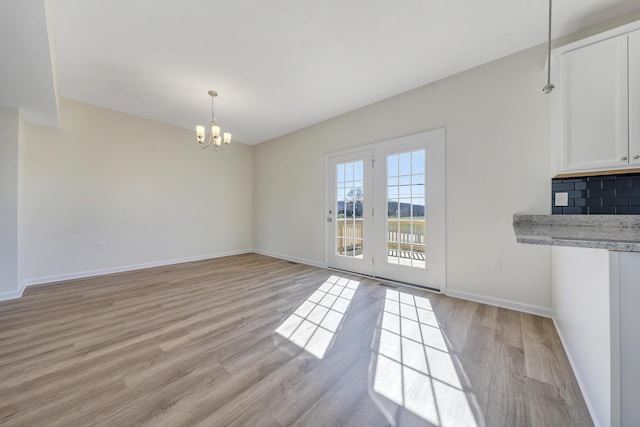 unfurnished dining area featuring light wood-style floors, baseboards, and an inviting chandelier