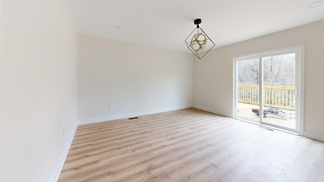 spare room with an inviting chandelier and light hardwood / wood-style flooring