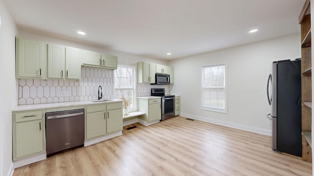 kitchen with light wood-type flooring, stainless steel appliances, backsplash, sink, and green cabinetry