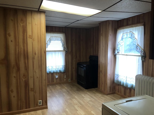 office area with a drop ceiling, light wood-type flooring, a wood stove, wooden walls, and radiator