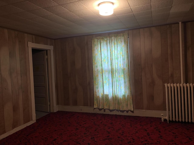 carpeted spare room featuring wood walls and radiator heating unit