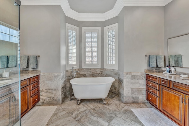 full bathroom with vanity, a freestanding tub, ornamental molding, wainscoting, and tile walls