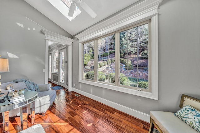 living area featuring a ceiling fan, vaulted ceiling with skylight, wood finished floors, and baseboards