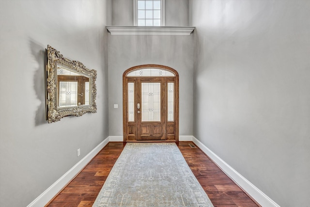 entryway featuring dark wood-style floors, baseboards, and a towering ceiling