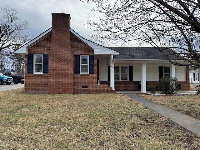 view of front facade featuring brick siding, crawl space, a chimney, and a front yard