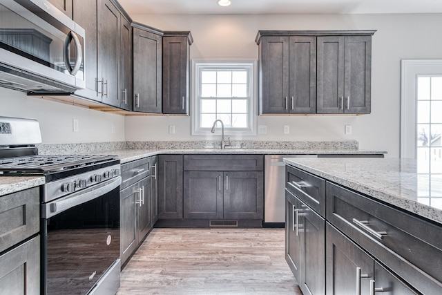 kitchen featuring light stone counters, a sink, stainless steel appliances, dark brown cabinetry, and light wood-type flooring