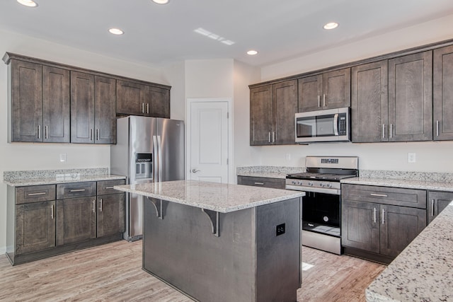 kitchen with dark brown cabinetry, appliances with stainless steel finishes, a kitchen island, and light wood-style floors