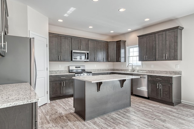 kitchen with a kitchen bar, a kitchen island, dark brown cabinetry, appliances with stainless steel finishes, and light wood finished floors