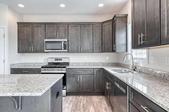 kitchen with dark brown cabinetry, appliances with stainless steel finishes, light stone counters, and a sink