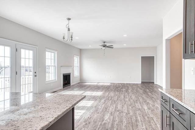 unfurnished living room featuring baseboards, light wood-type flooring, recessed lighting, a fireplace, and ceiling fan with notable chandelier