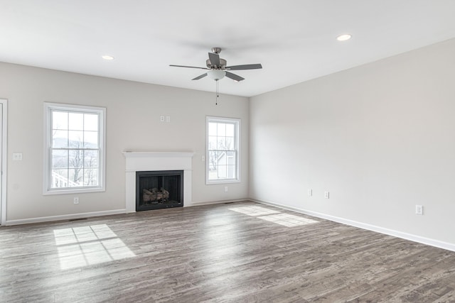 unfurnished living room featuring a fireplace, a ceiling fan, baseboards, and wood finished floors