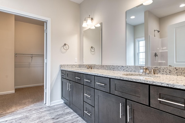 full bathroom featuring a spacious closet, double vanity, a shower, and a sink