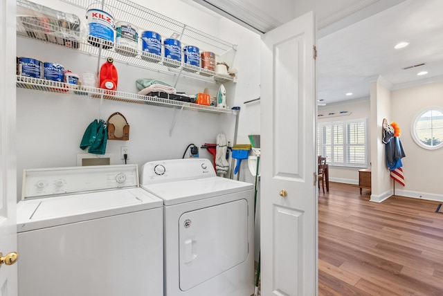 clothes washing area with washing machine and dryer, crown molding, and hardwood / wood-style floors