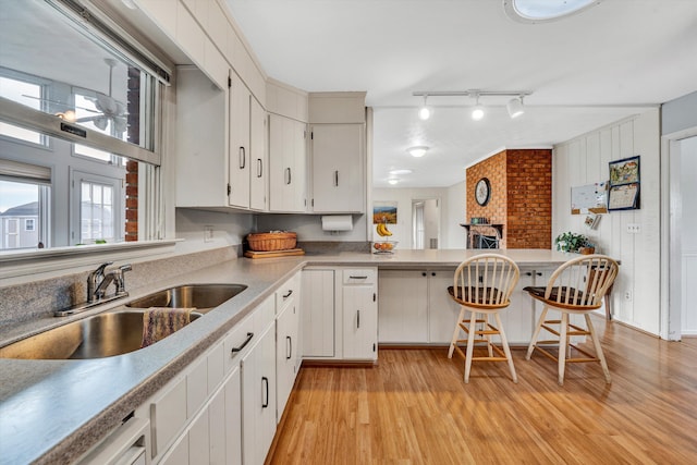 kitchen featuring a breakfast bar, a peninsula, light wood-style floors, white cabinets, and a sink