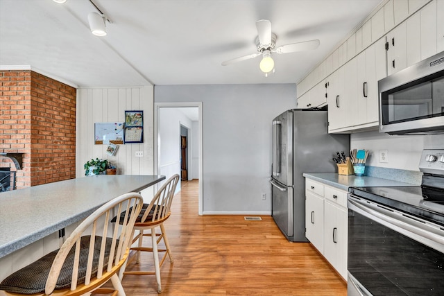 kitchen with a breakfast bar, light wood-type flooring, appliances with stainless steel finishes, white cabinets, and a ceiling fan