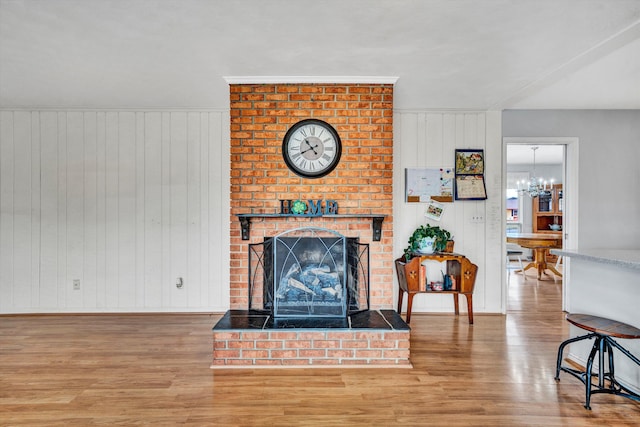 living room featuring baseboards, a notable chandelier, a brick fireplace, and wood finished floors