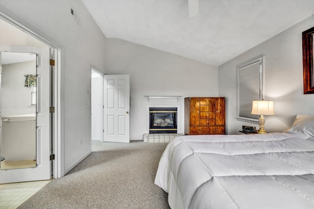 carpeted bedroom with a glass covered fireplace, vaulted ceiling, and ceiling fan