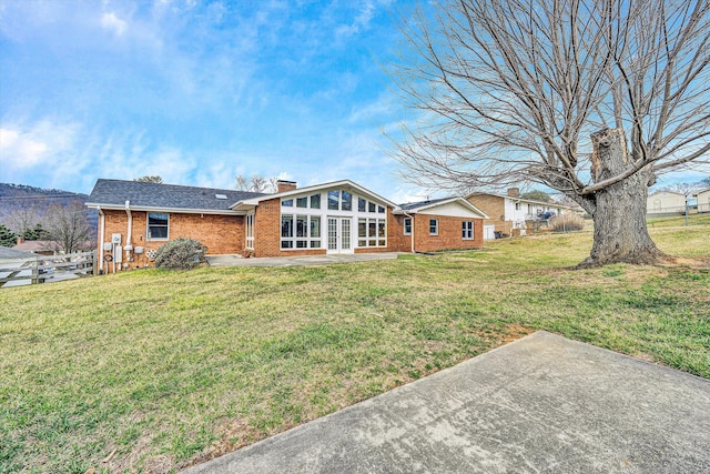 rear view of property featuring french doors, a yard, a shingled roof, brick siding, and a chimney