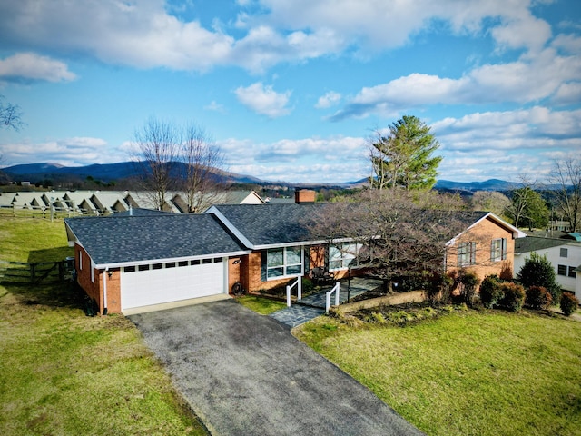 ranch-style house featuring a front yard, driveway, an attached garage, brick siding, and a mountain view