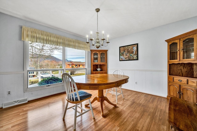 dining space featuring a notable chandelier, visible vents, a wainscoted wall, and wood finished floors