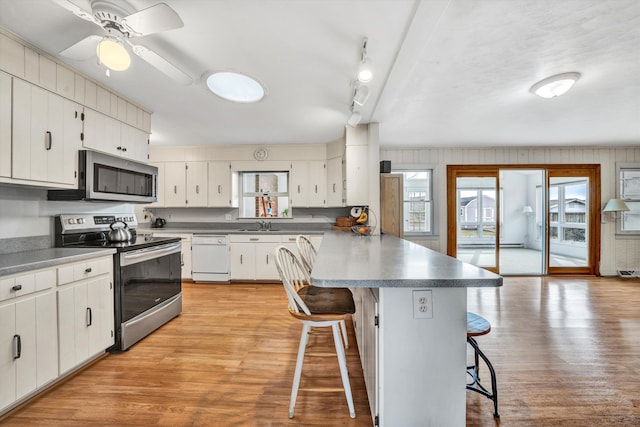 kitchen featuring a breakfast bar area, a peninsula, stainless steel appliances, light wood-style floors, and white cabinetry