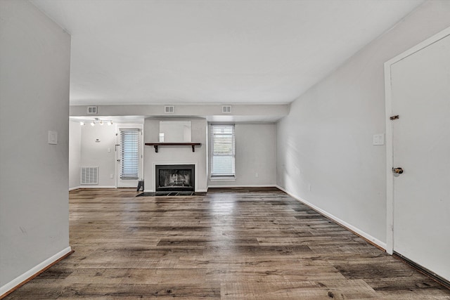 unfurnished living room featuring baseboards, visible vents, a fireplace with flush hearth, and dark wood-type flooring