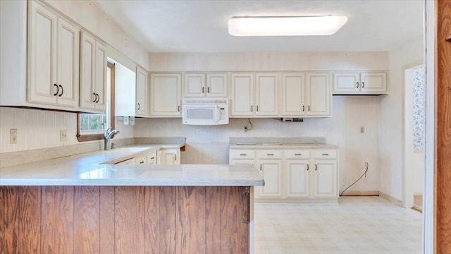 kitchen with white microwave, a peninsula, a sink, light countertops, and light floors