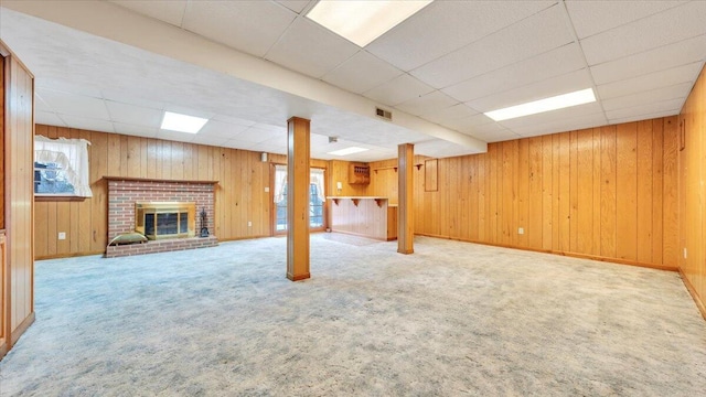 below grade area featuring a paneled ceiling, a brick fireplace, carpet flooring, and visible vents