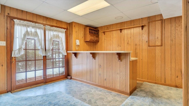 interior space featuring a bar, a paneled ceiling, and wooden walls