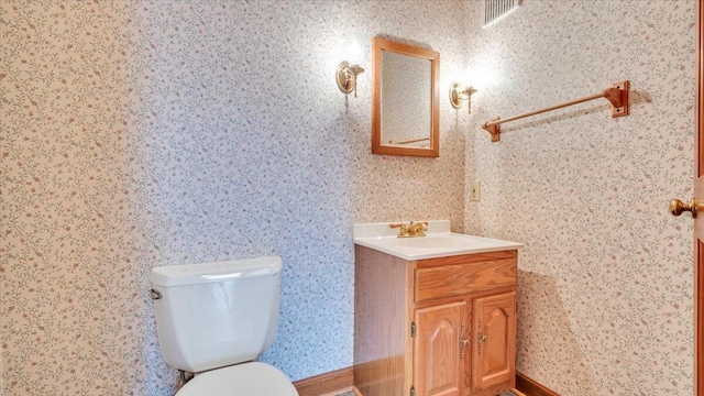 half bathroom featuring visible vents, vanity, toilet, and wallpapered walls