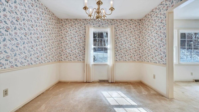 empty room with wainscoting, a notable chandelier, light carpet, and wallpapered walls