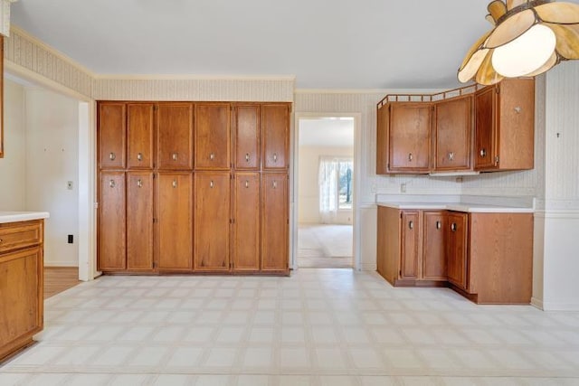 kitchen with light floors, light countertops, brown cabinetry, and wallpapered walls