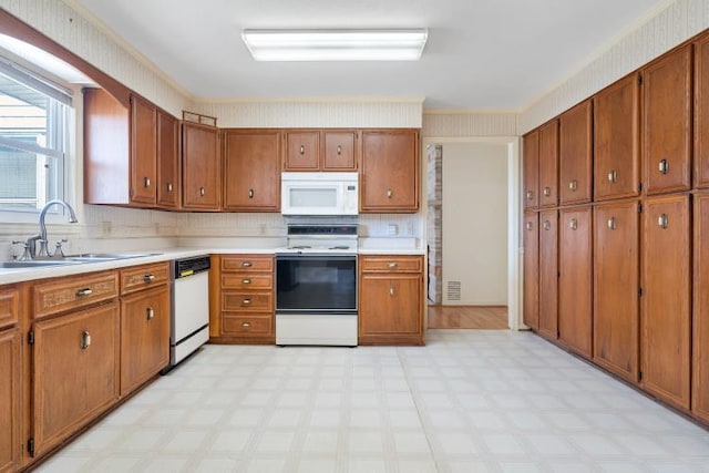 kitchen featuring white appliances, brown cabinetry, light floors, wallpapered walls, and a sink