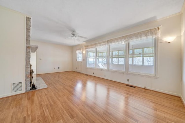 unfurnished living room with visible vents, a fireplace with raised hearth, wood finished floors, and a ceiling fan