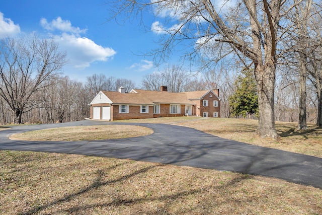 ranch-style home with aphalt driveway, a front yard, a garage, brick siding, and a chimney