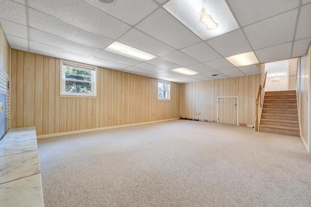 basement with stairs, a paneled ceiling, and wood walls