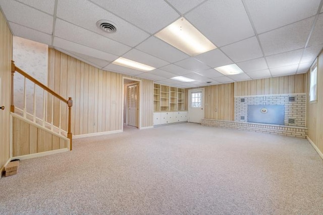 below grade area with wooden walls, visible vents, carpet floors, stairs, and a brick fireplace