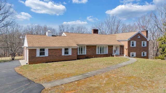 view of front of home with a shingled roof, a front yard, brick siding, and aphalt driveway