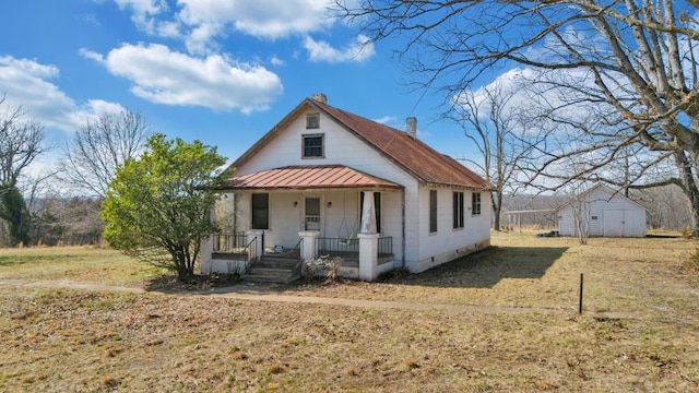 bungalow-style home featuring a standing seam roof, covered porch, an outdoor structure, metal roof, and a chimney